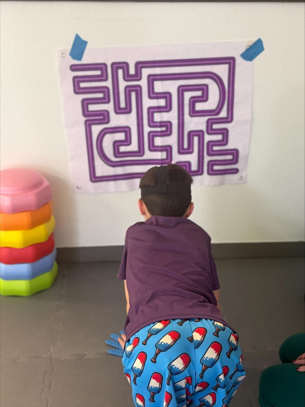 Child on hands and knees tracing a wall maze with a headlamp at NeuroNest Pediatric Therapy